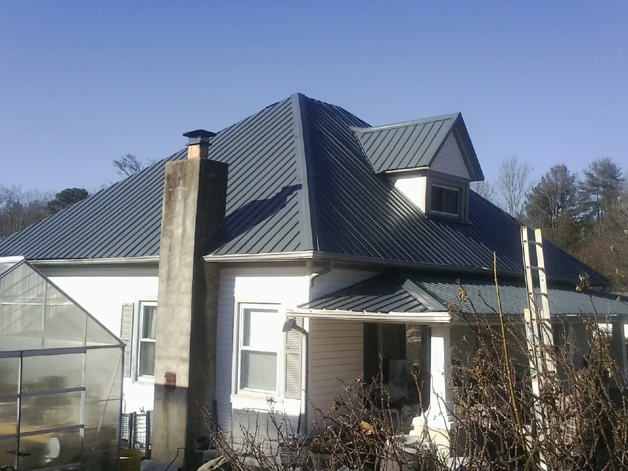 Dark blue standing seam metal roof on a white farmhouse with dormer — Slate & Tile Roof Repair by Roofing Brothers in Willard