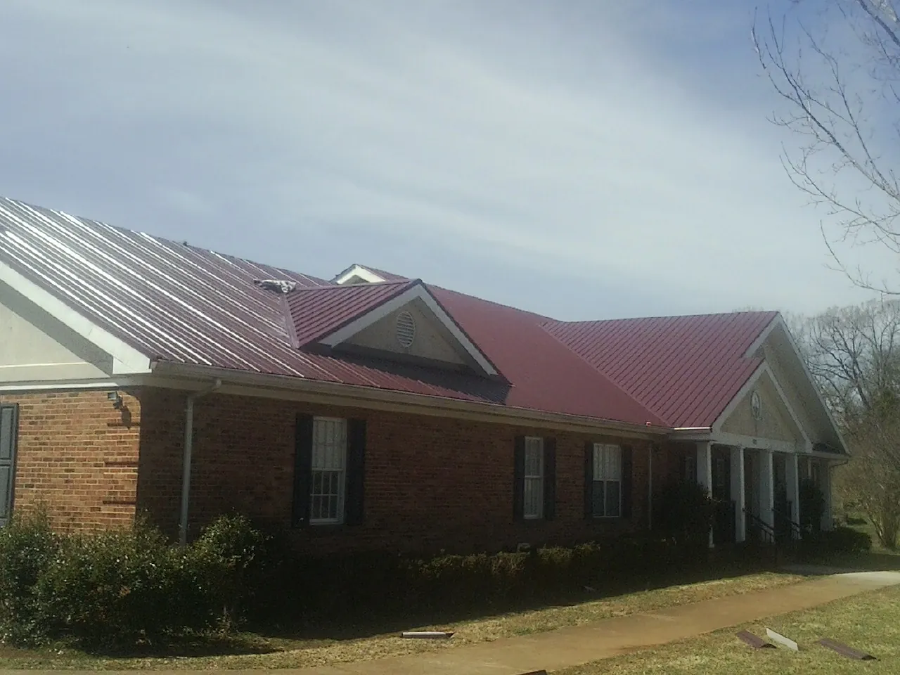 Red metal roof with gabled entries on a long brick building, from a Hail Damage Roof Repair job in Willard