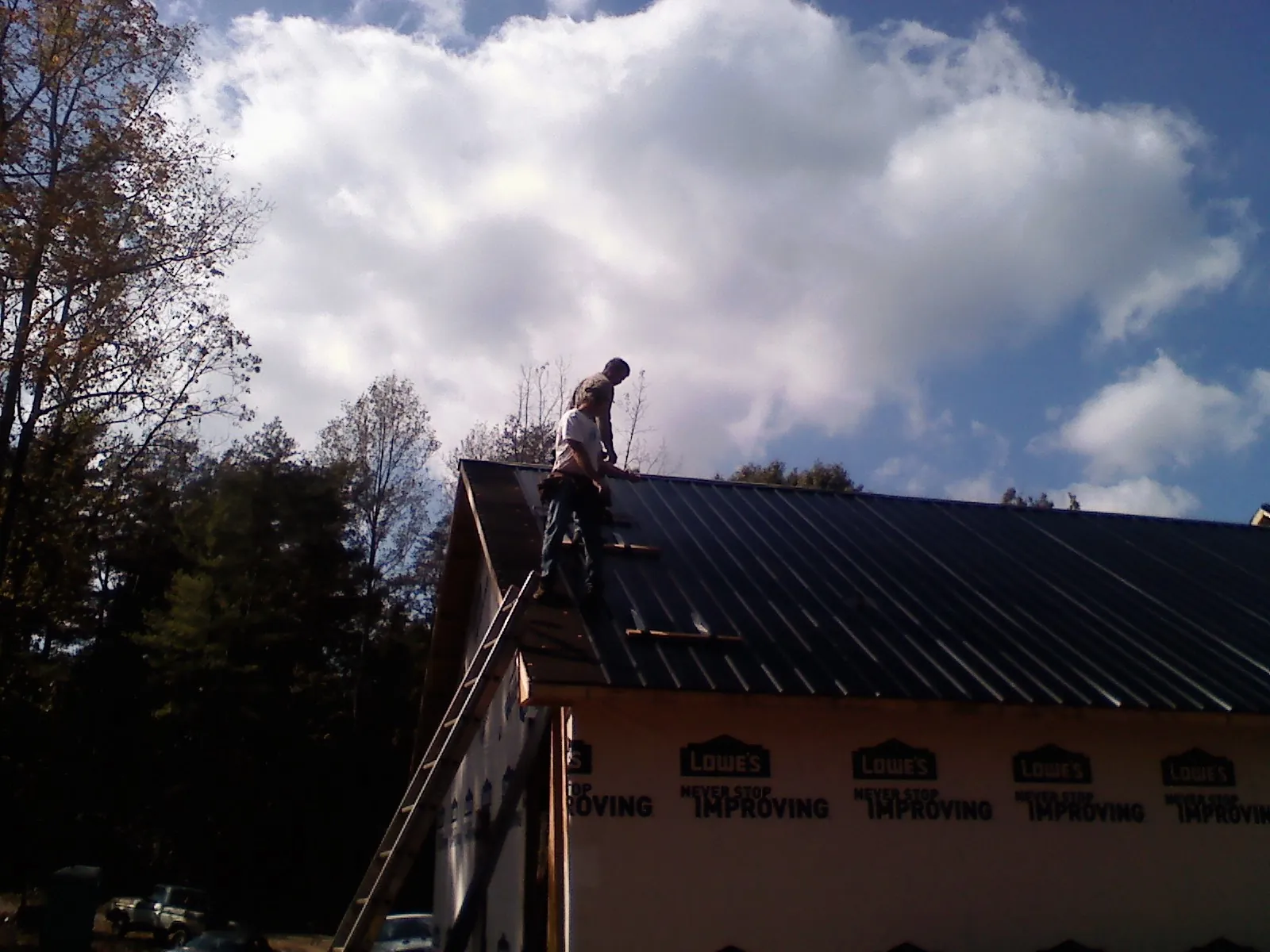 Roofer fastening dark metal panels high against a cloudy sky, from a Roof Inspection job in Willard