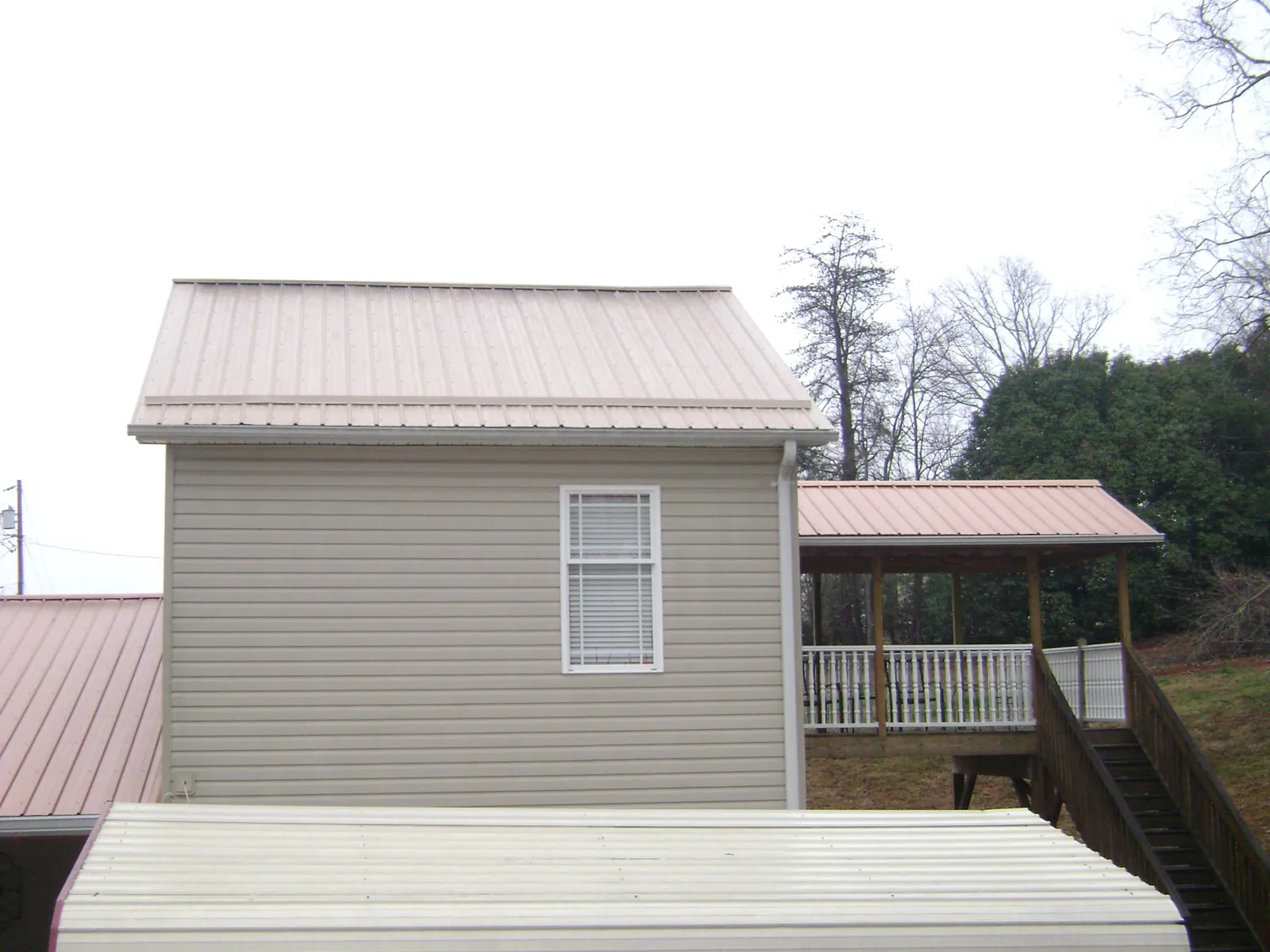 Tan metal roofs on a two story addition and attached porch, from a Roof Replacement job in Willard